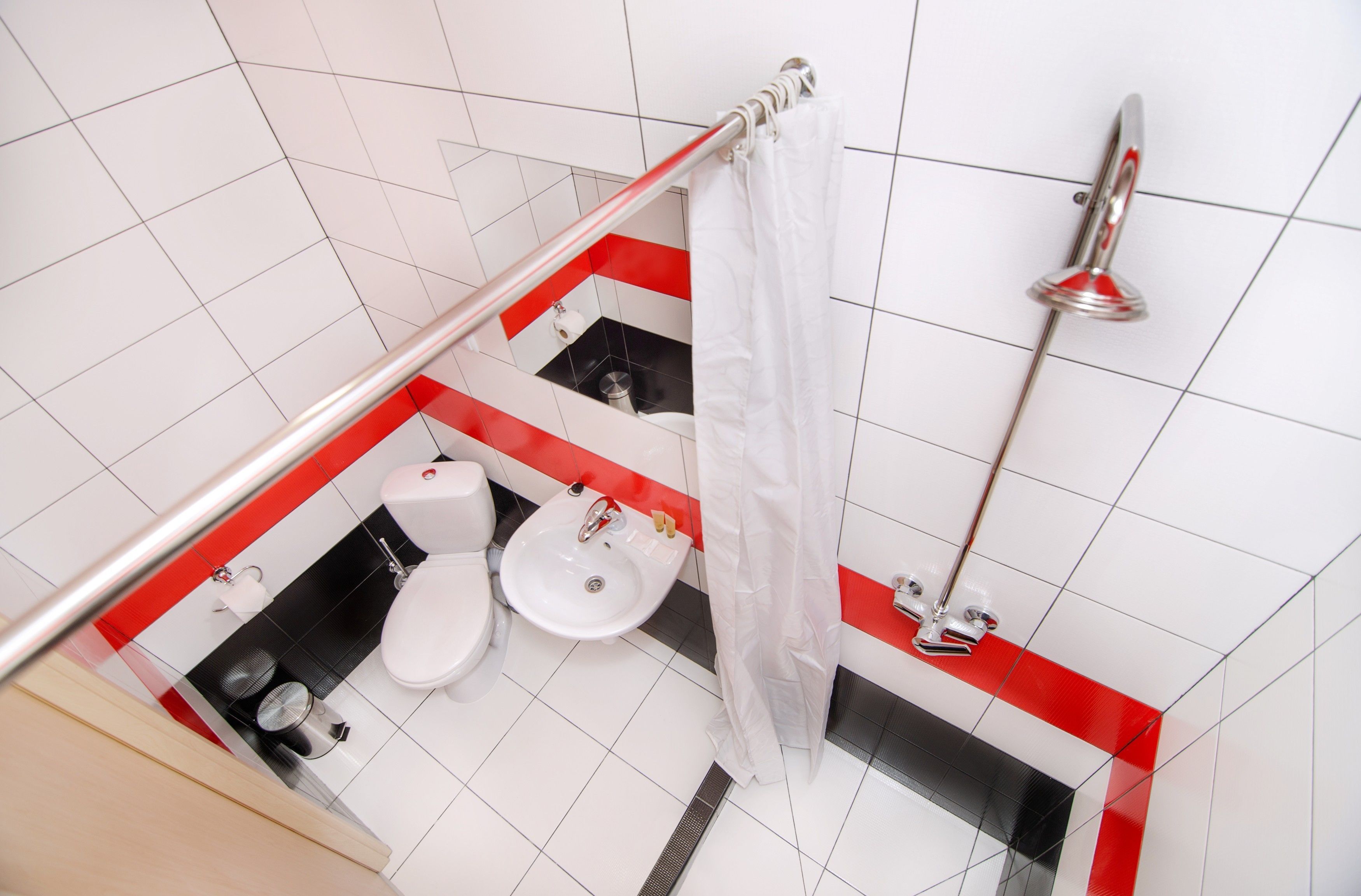 Un baño con lavamanos, inodoro y zona de ducha, con un diseño de azulejos rojos y negros.