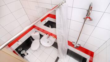 Un baño con lavamanos, inodoro y zona de ducha, con un diseño de azulejos rojos y negros.