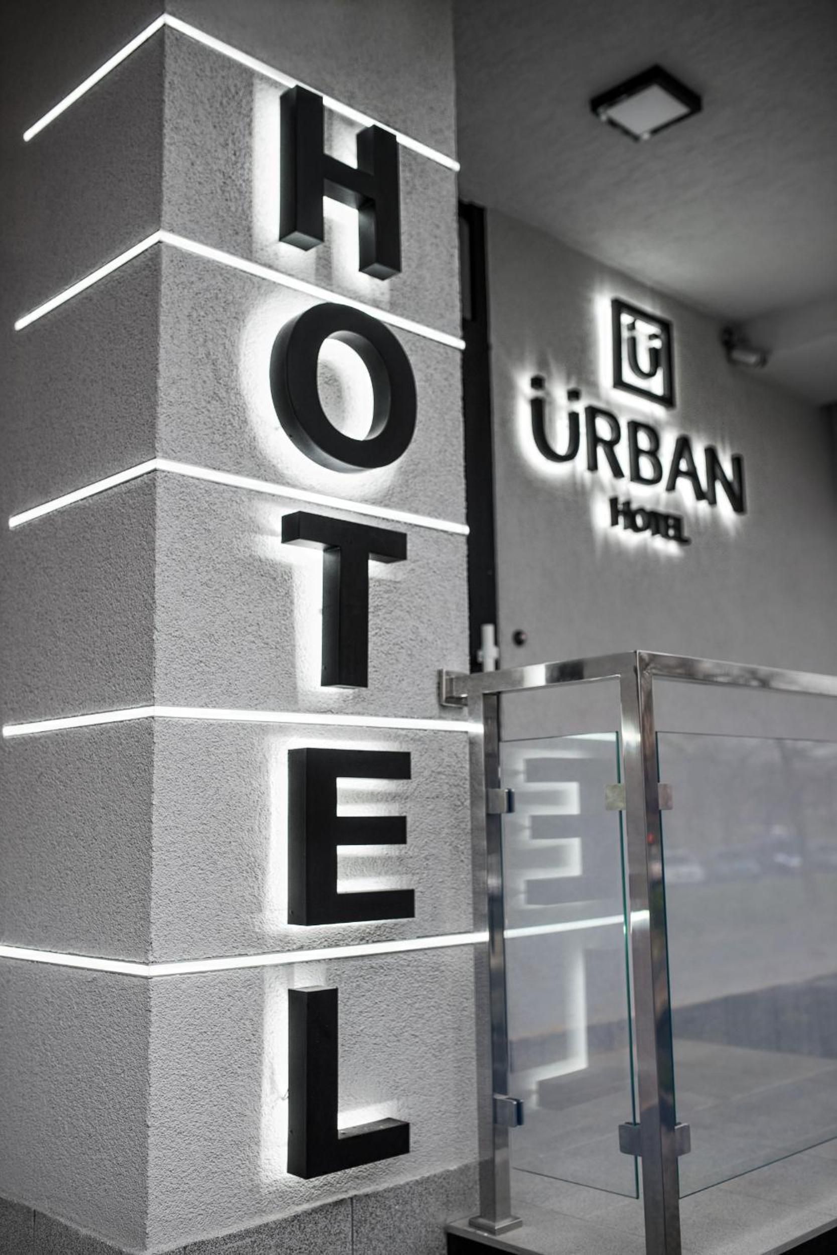 A hotel entrance with a modern design, featuring a prominent 'HOTEL' sign and the name 'URBAN HOTEL' on the wall.