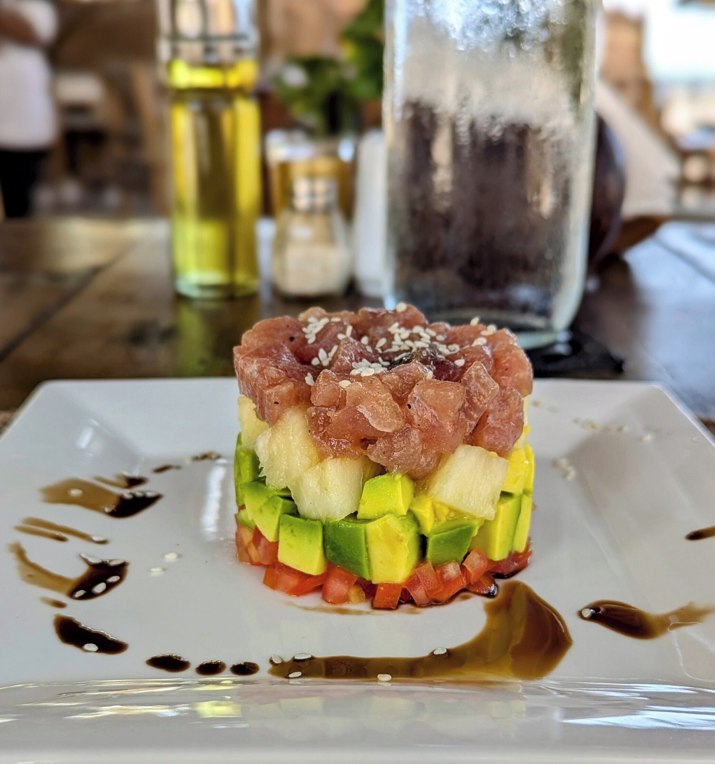 A dish with avocado, tomato, and tuna on a white plate.