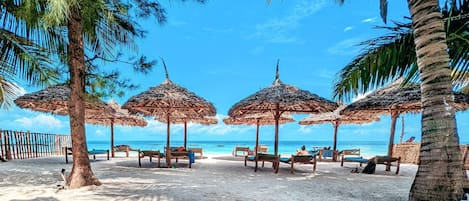 Een privéstrand, ligstoelen aan het strand, parasols, een strandbar