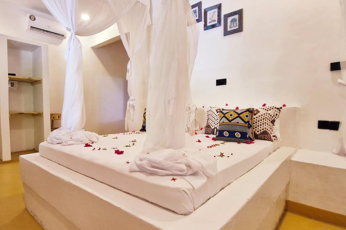 A bedroom with a canopy bed, white bedding, and a decorative pillow.