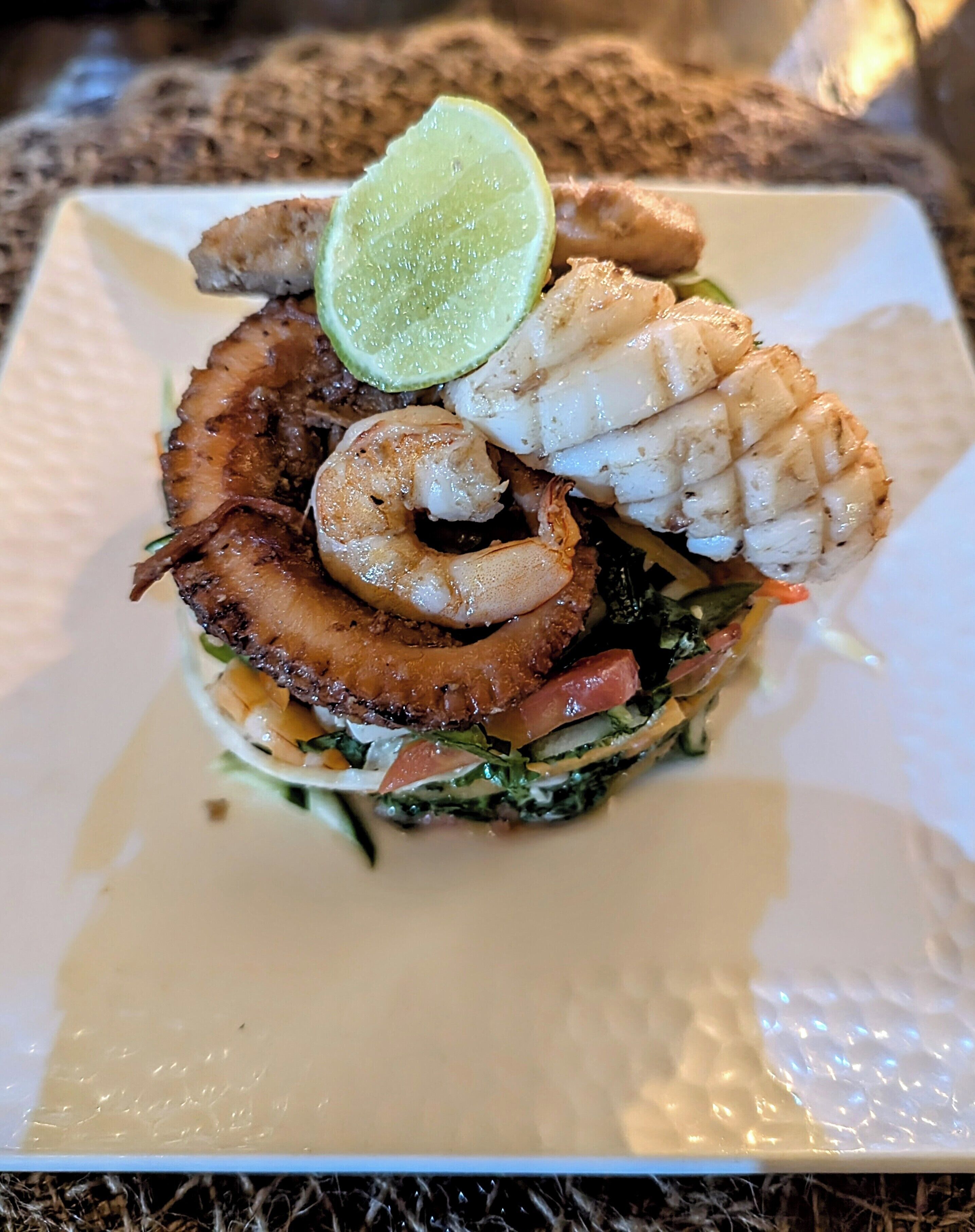 A seafood burger with grilled shrimp and crab on a white plate.