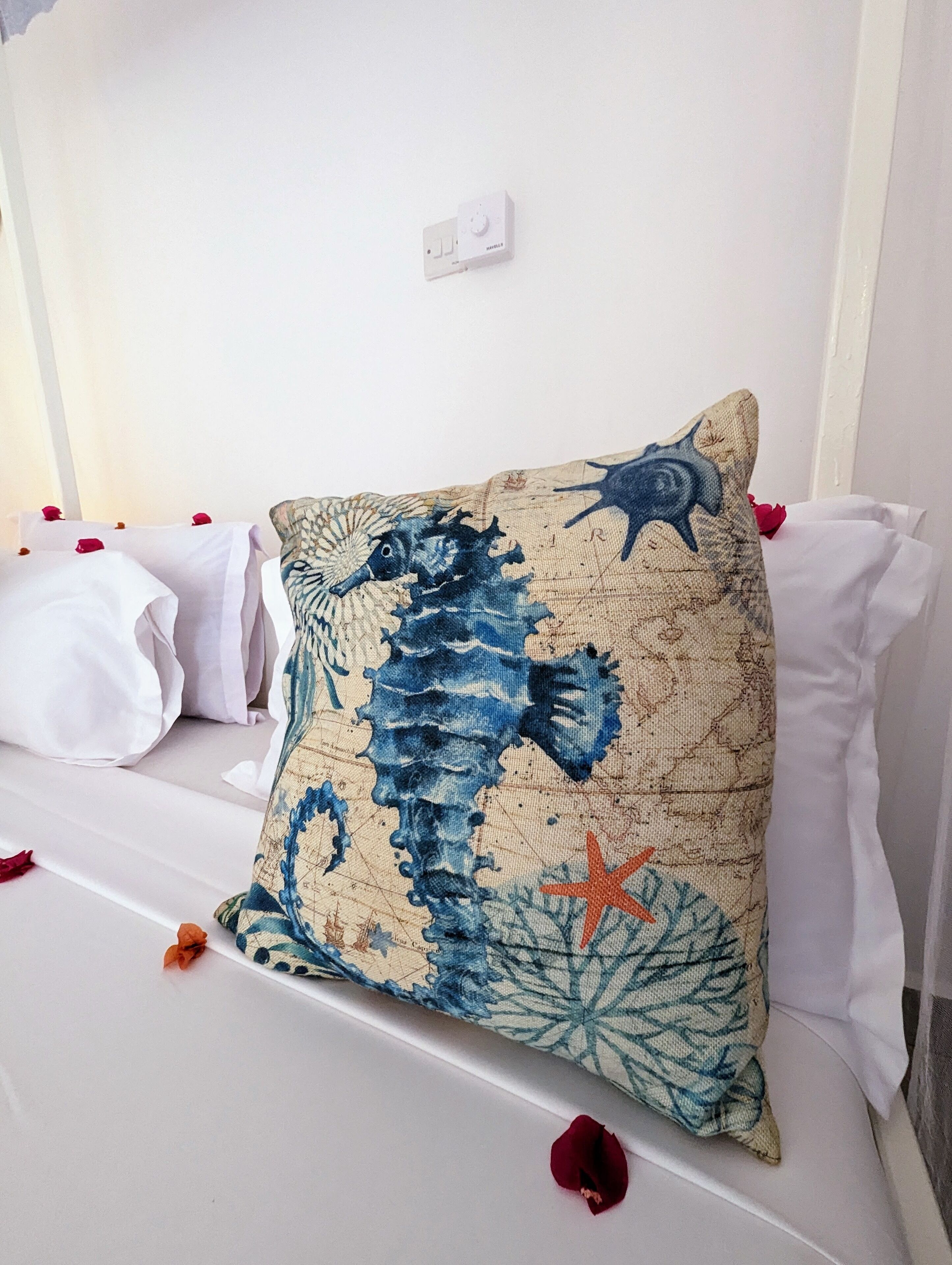 Een bed met witte lakens, een sierkussen met zeepaardjes en rozenblaadjes verspreid over het bed.