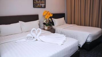 A hotel room with two beds, white linens, a heart-shaped towel arrangement, a vase with yellow flowers, and a painting on the wall.