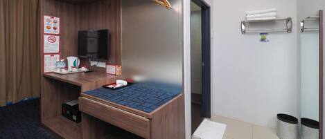 Hotelkamer met een houten bed, een televisie, een klein bureau met een dienblad toiletartikelen, een handdoekrek en een prullenbak.