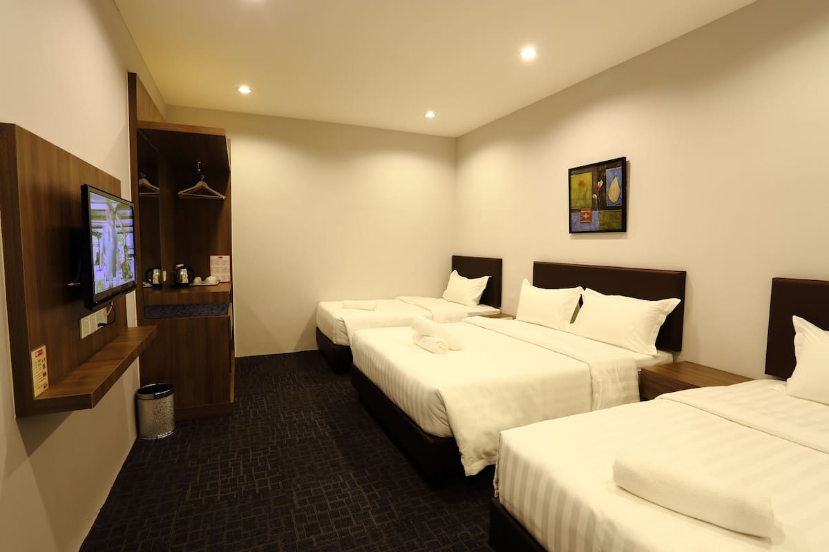 Habitación de hotel con tres camas, un televisor, perchero y un cuadro en la pared.
