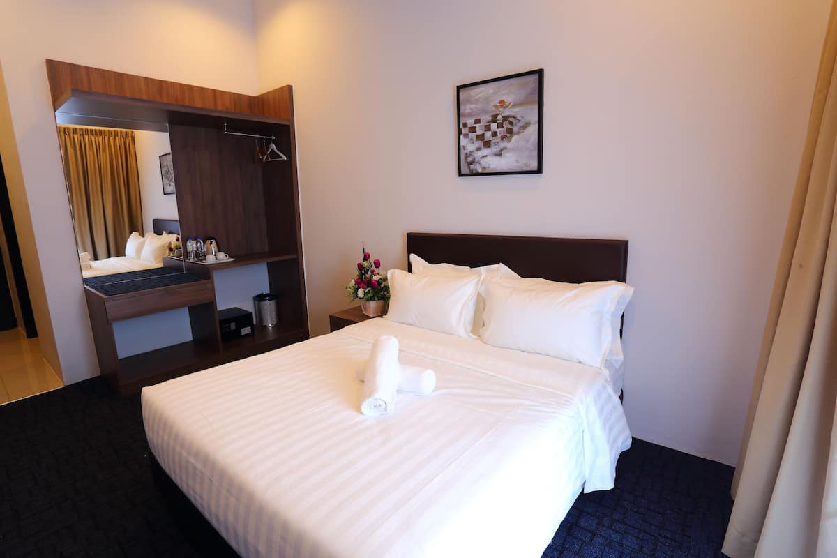 Habitación de hotel con cama, escritorio con espejo, mesita de noche con un florero y un cuadro en la pared.