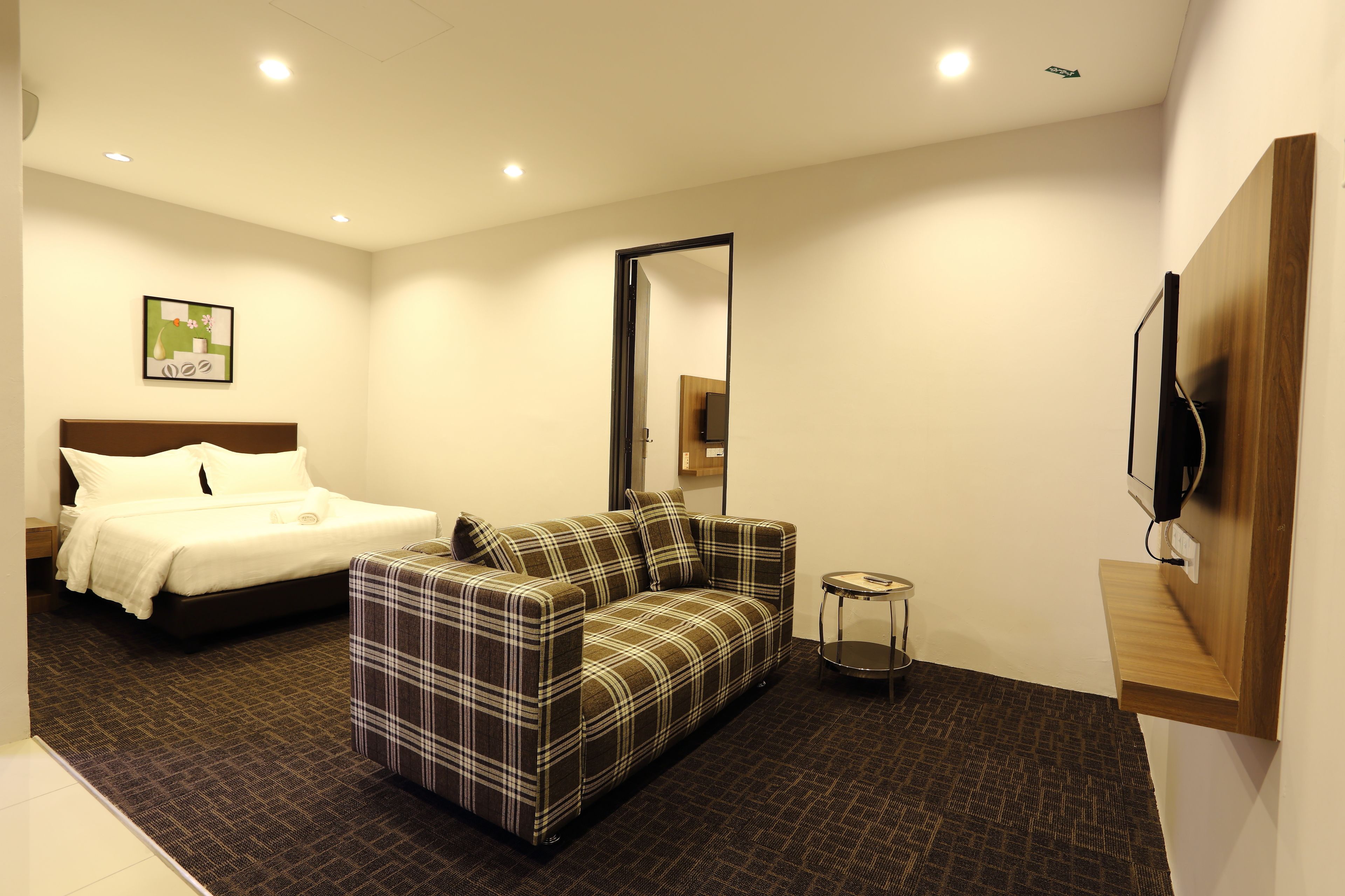 Una habitación de hotel moderna con una cama, un sofá, una mesita pequeña y un televisor montado en la pared.
