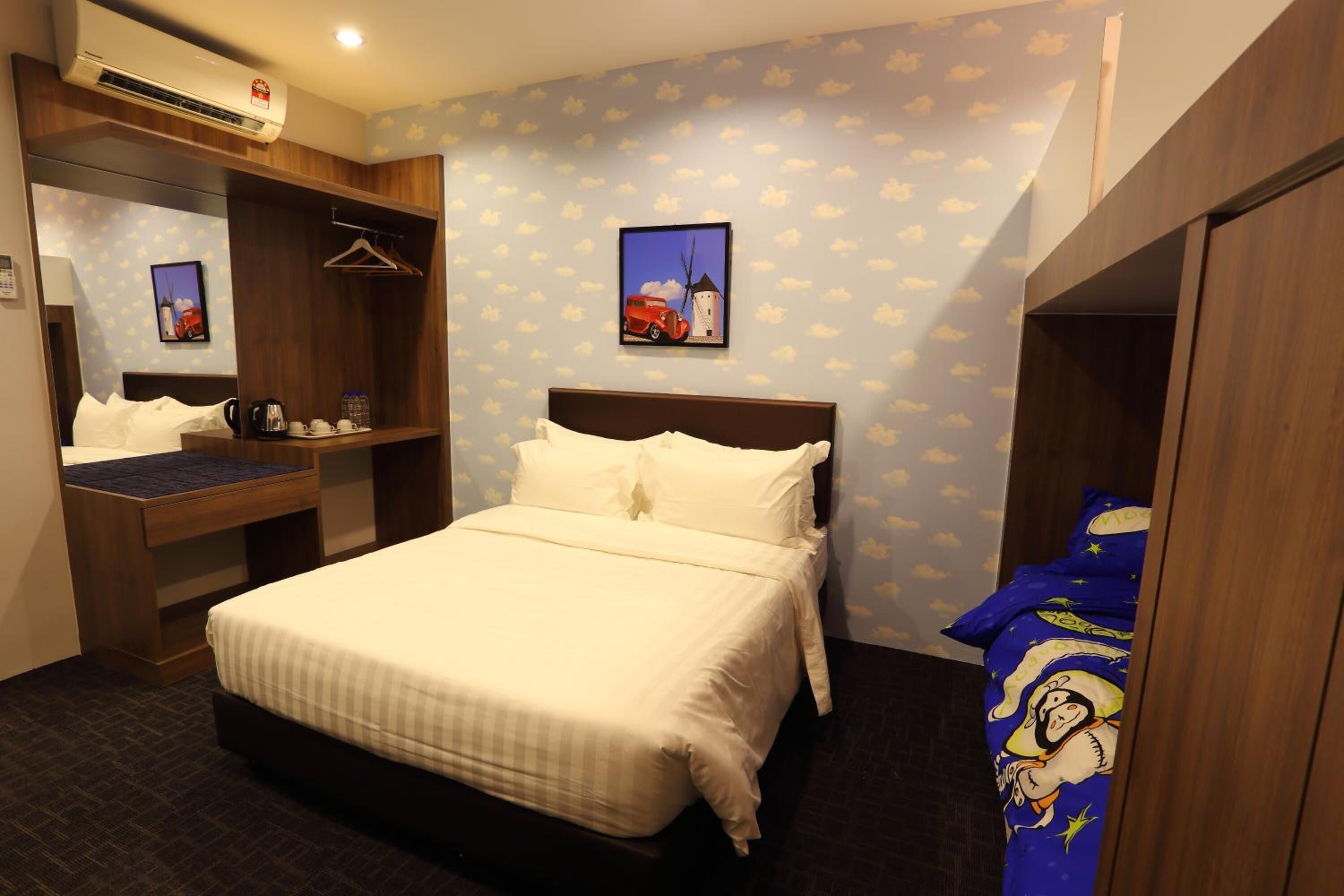 Quarto de hotel com cama, escrivaninha, armário e televisão presa à parede.