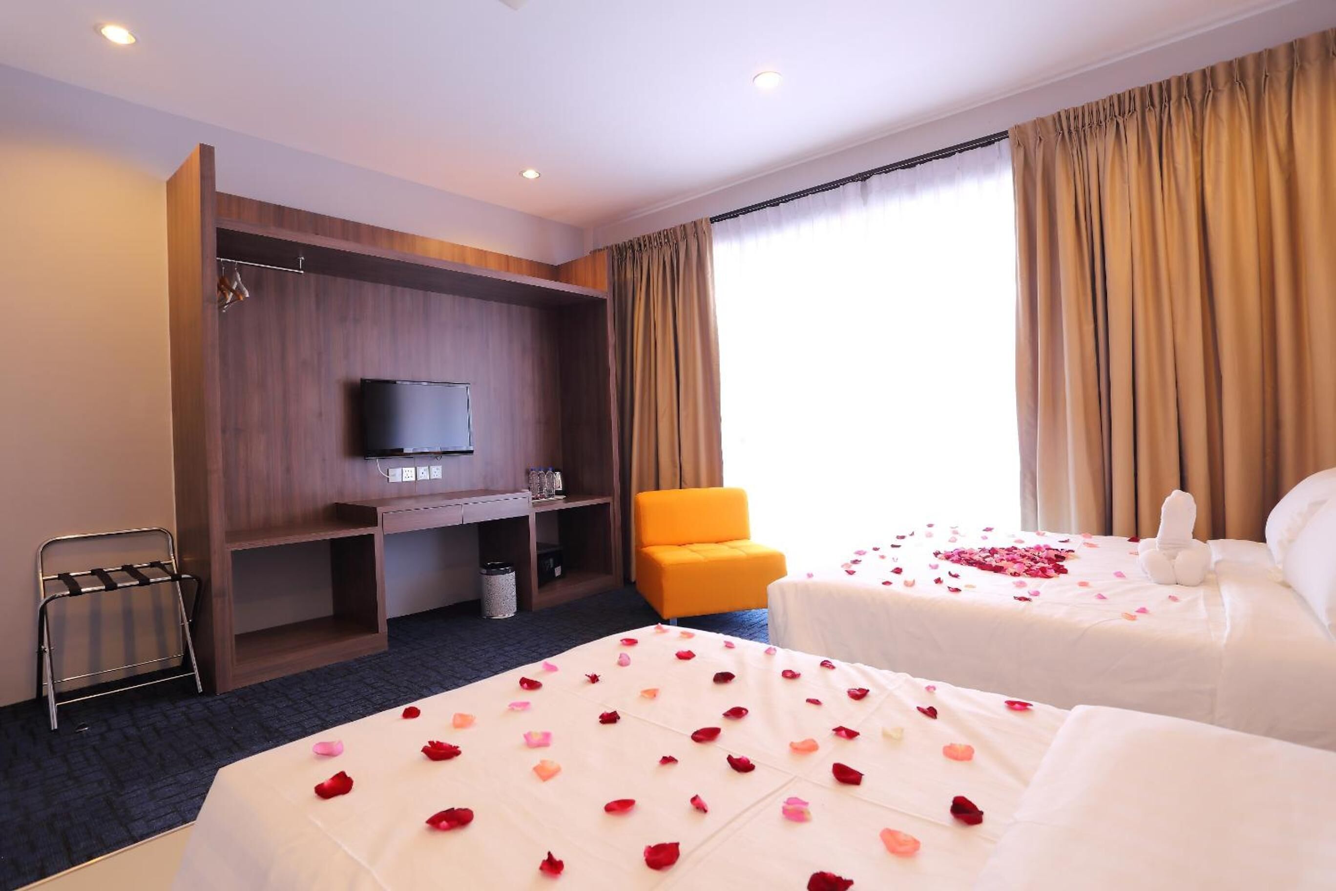 A hotel room with two beds, a TV, a desk, a chair, and a window with curtains.