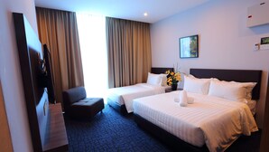Quarto de hotel com duas camas, uma escrivaninha, uma cadeira e uma janela grande com cortinas.