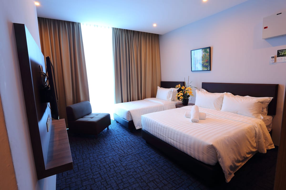 Habitación de hotel con dos camas, un escritorio, una silla y un ventanal con cortinas.