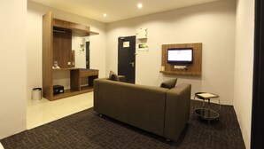 Quarto de hotel moderno com sofá, uma pequena mesa, TV fixada na parede e um guarda-roupa de madeira.