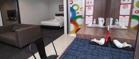 A hotel room with a bed, a sofa, a desk with a computer, and a bathroom with a shower and toilet.