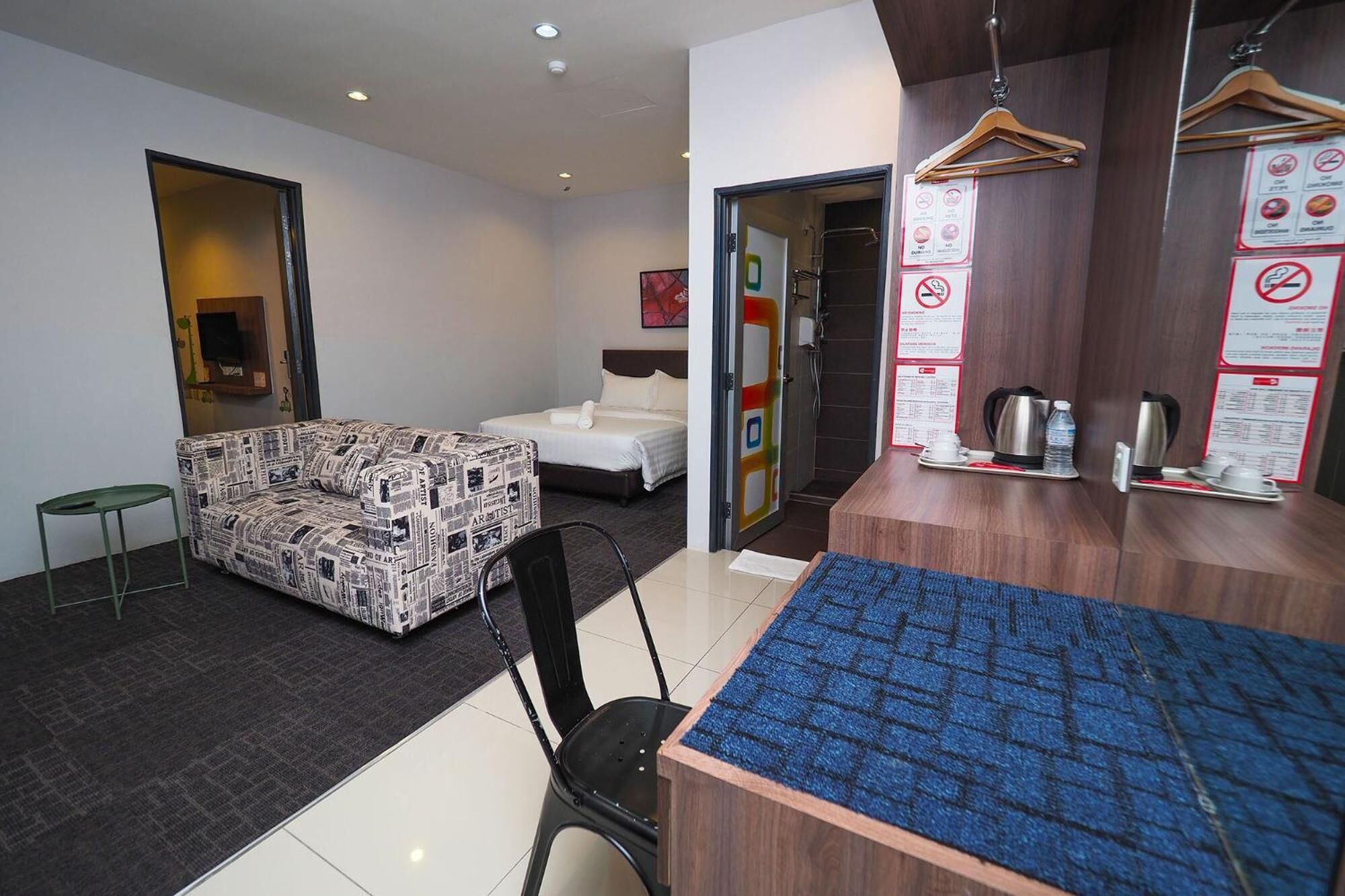 Habitación de hotel con sofá, cama, una mesita con bandeja, silla y mostrador de recepción con alfombra azul.