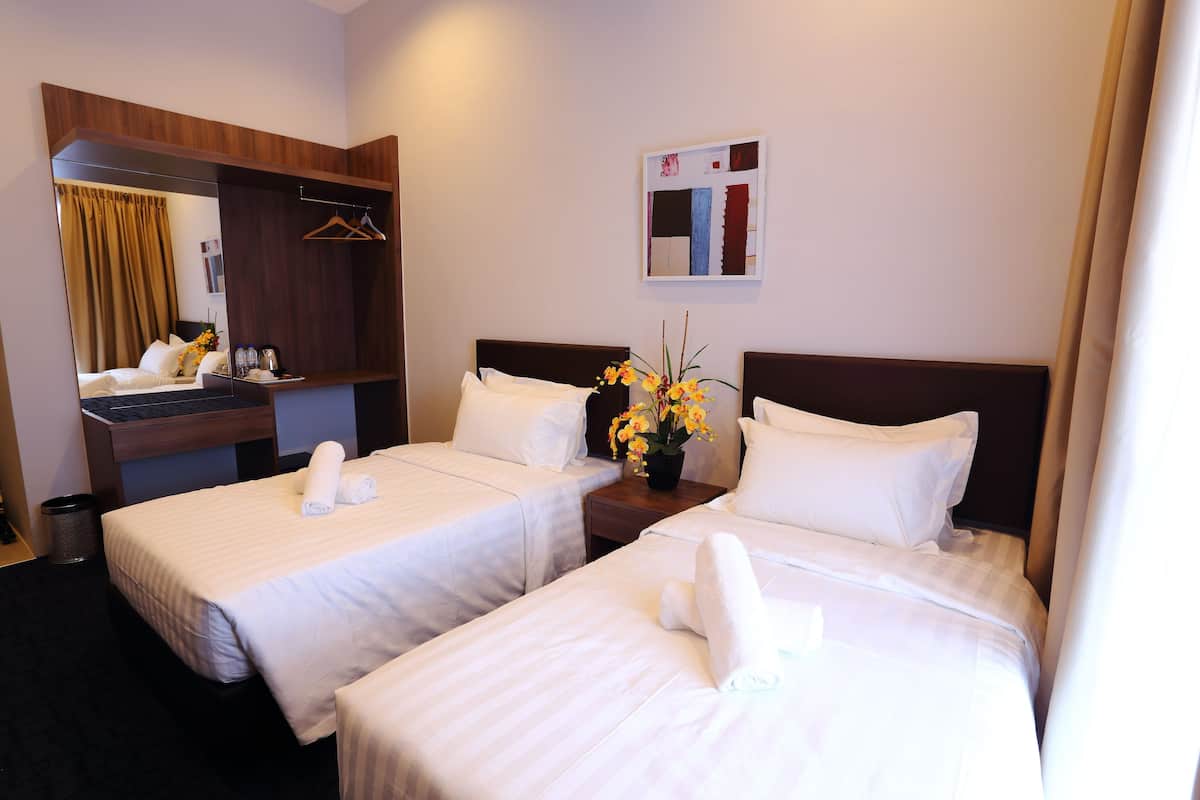 Una habitación de hotel con dos camas, un escritorio, un espejo y un jarrón con flores.
