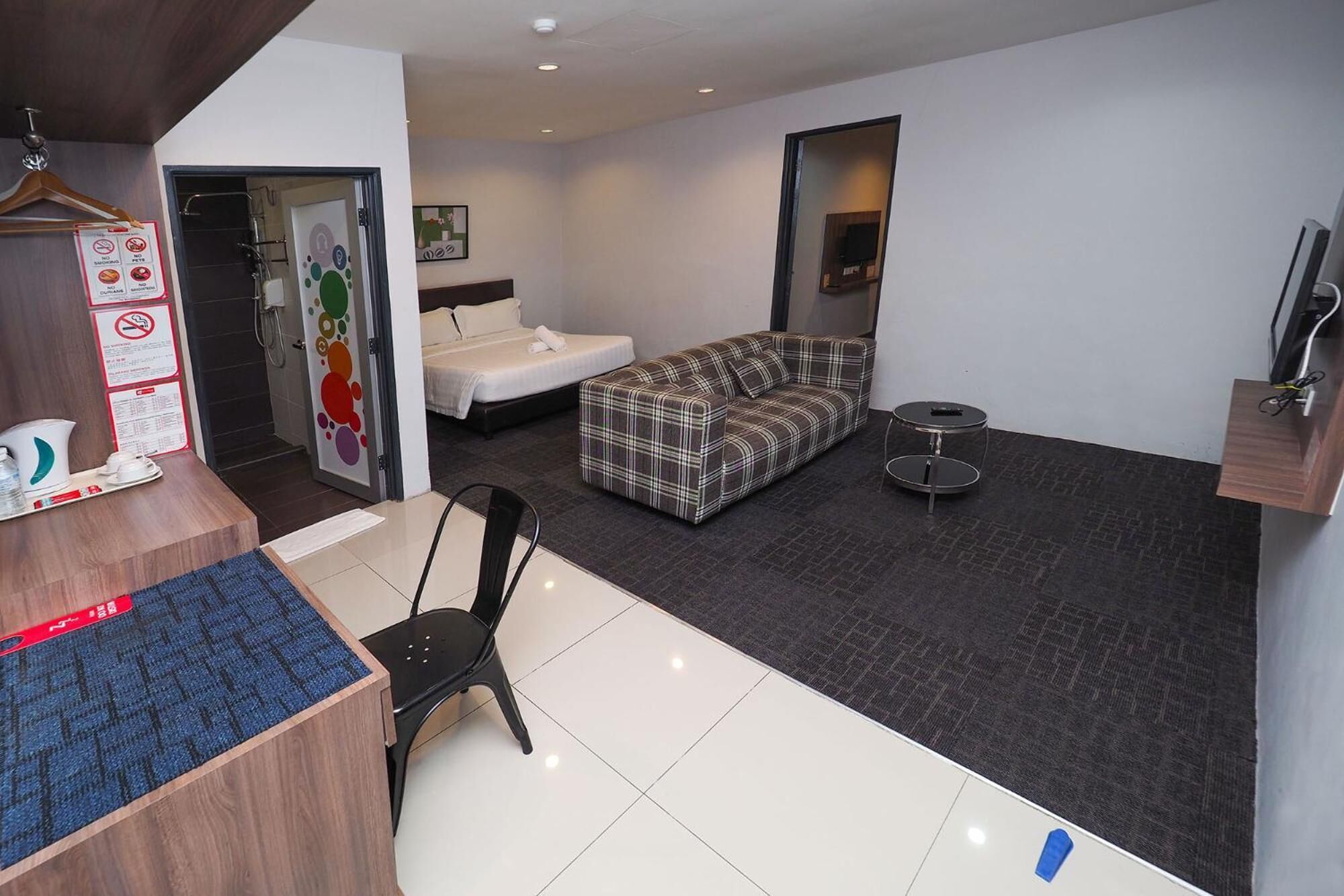 A hotel room with a bed, a sofa, a desk with a chair, a small round table, and a TV mounted on the wall.