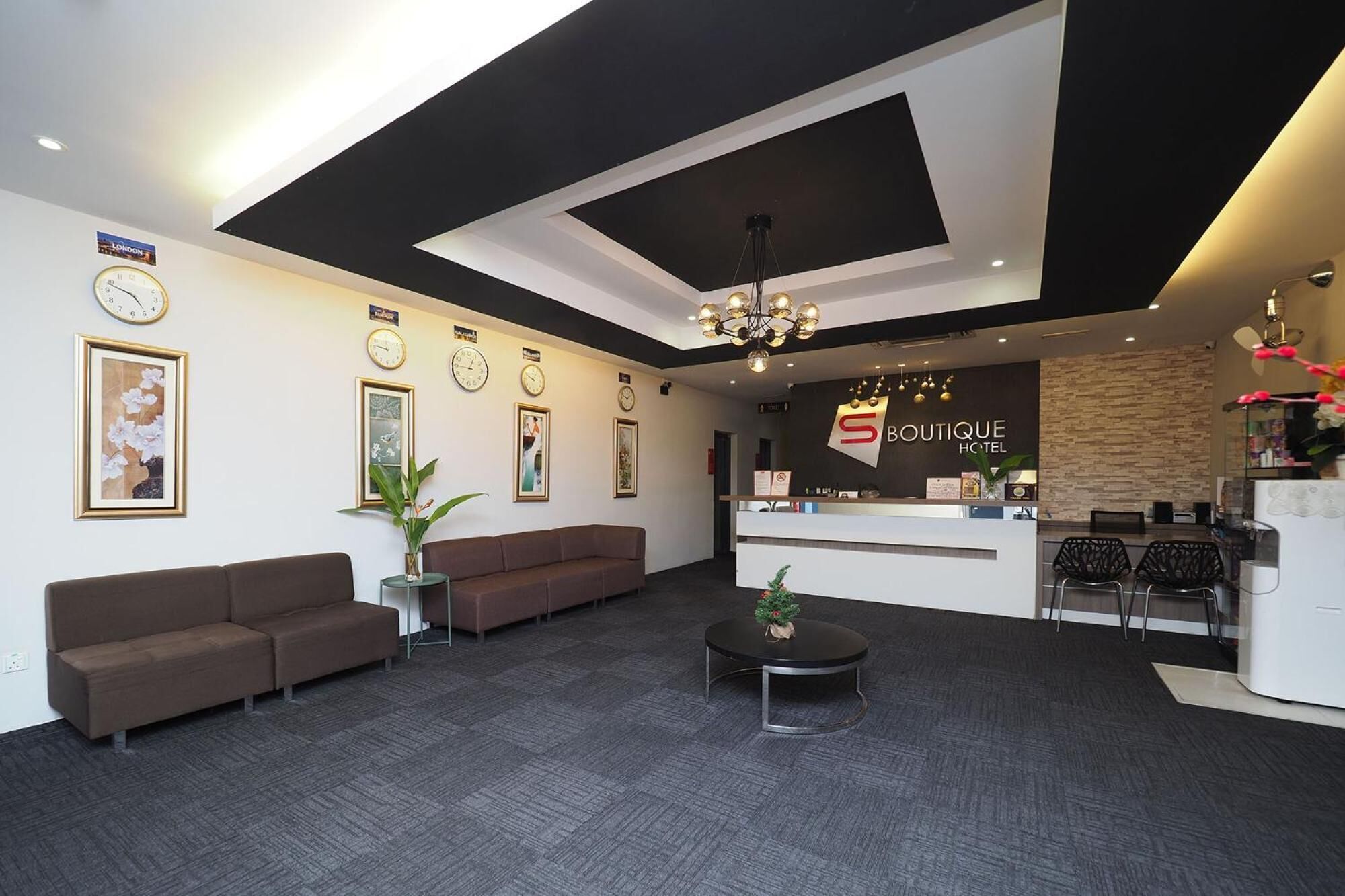 A modern hotel lobby with a reception desk, sofas, a chandelier, and clocks on the wall.