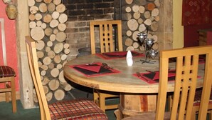 A round wooden table with red placemats, surrounded by wooden chairs with cushioned seats. A white candle holder is placed on the table. - The Brewers Arms (South Petherton)