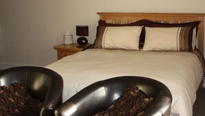 A neatly made bed with a wooden headboard, a bedside table with a lamp and a tissue box, and a wall with abstract art. - The Brewers Arms (South Petherton)