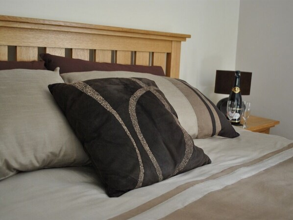 A bed with a wooden headboard, multiple pillows, and a bedside table with a lamp.