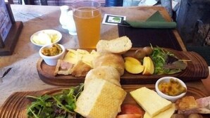 A wooden board with various food items including bread, cheese, apples, and greens. - The Brewers Arms (South Petherton)