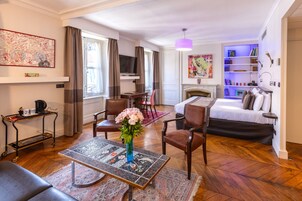 Quarto de hotel com cama, escrivaninha, poltrona, mesa de centro, televisão e lareira.