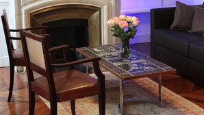 Uma sala de estar com lareira, uma mesa de centro com um vaso de flores, uma estante de livros e um sofá.