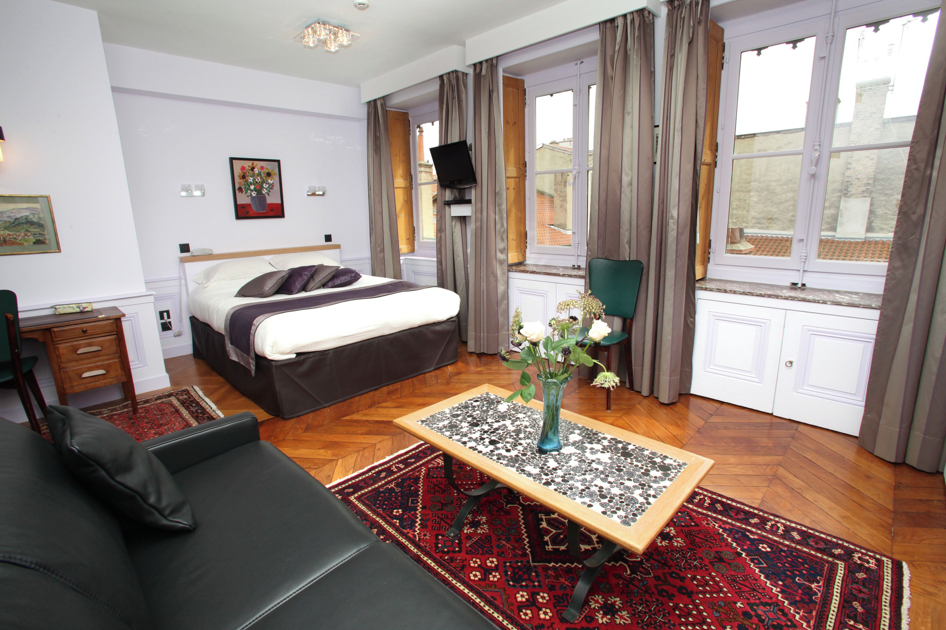 Et hotelværelse med seng, sofa, et bord med en vase og et vindue med gardiner.
