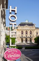 Un letrero de hotel con el nombre 'HOTEL des Celestins' y una vista de un edificio clásico al fondo.