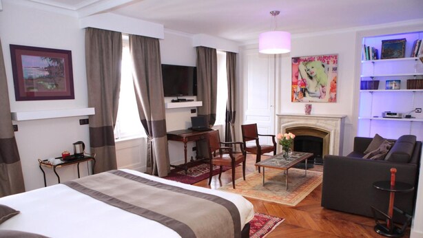Quarto de hotel com uma cama grande, uma mesa com um laptop, um sofá, uma lareira e uma estante de livros.