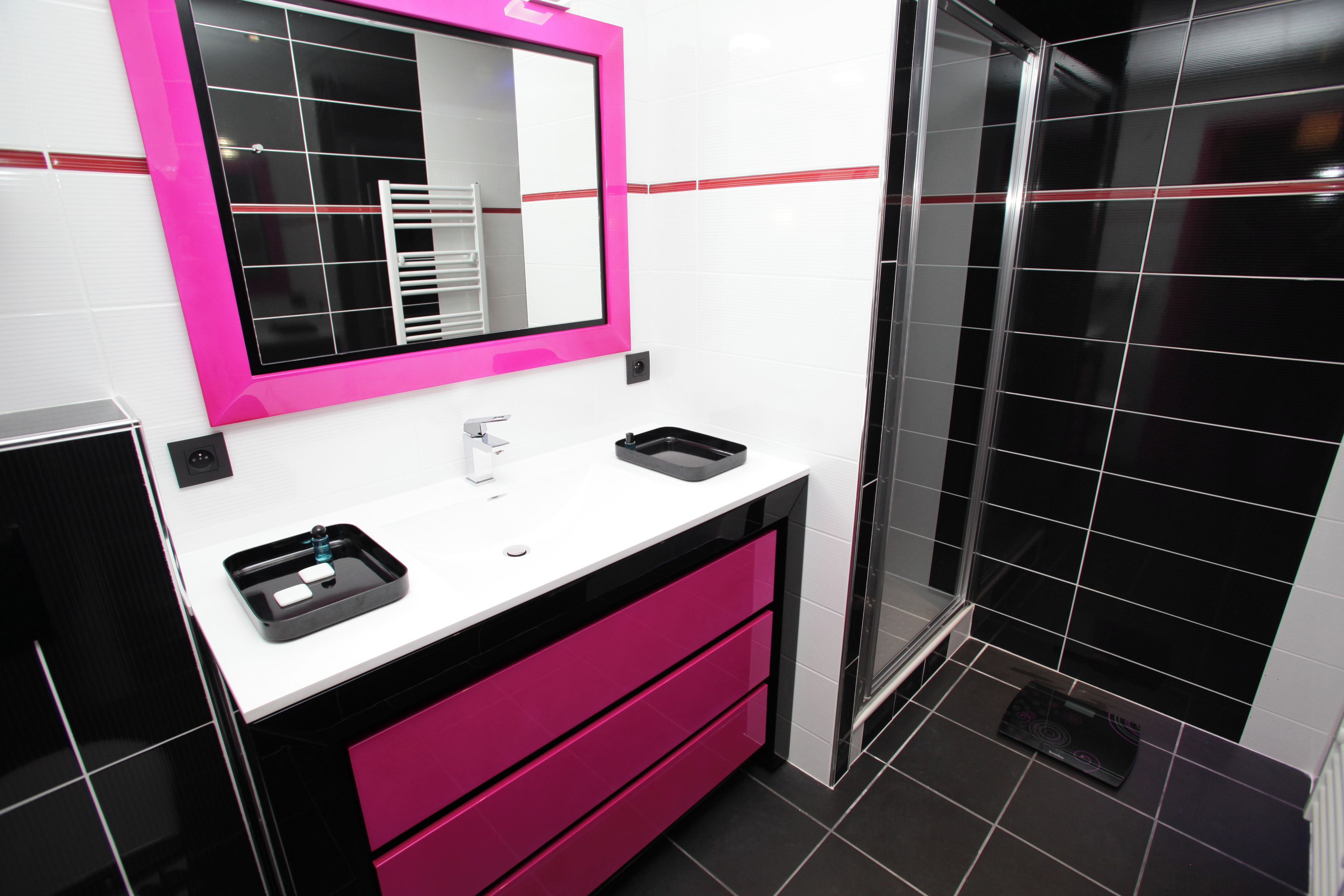 A modern bathroom with a white sink, a pink vanity, and a black tiled shower area.