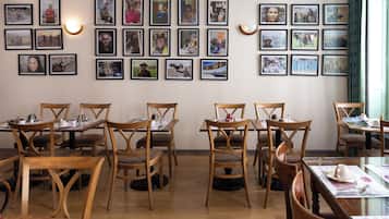 A dining area with wooden tables and chairs, a wall adorned with framed photographs, and a patterned wallpaper background.