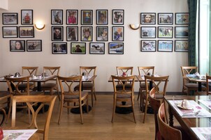 Un comedor con mesas y sillas de madera, una pared decorada con fotografías enmarcadas y un papel tapiz estampado.