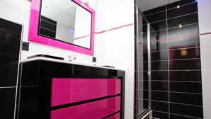 Um banheiro moderno com toucador preto e rosa, um espelho grande e box de chuveiro em vidro.