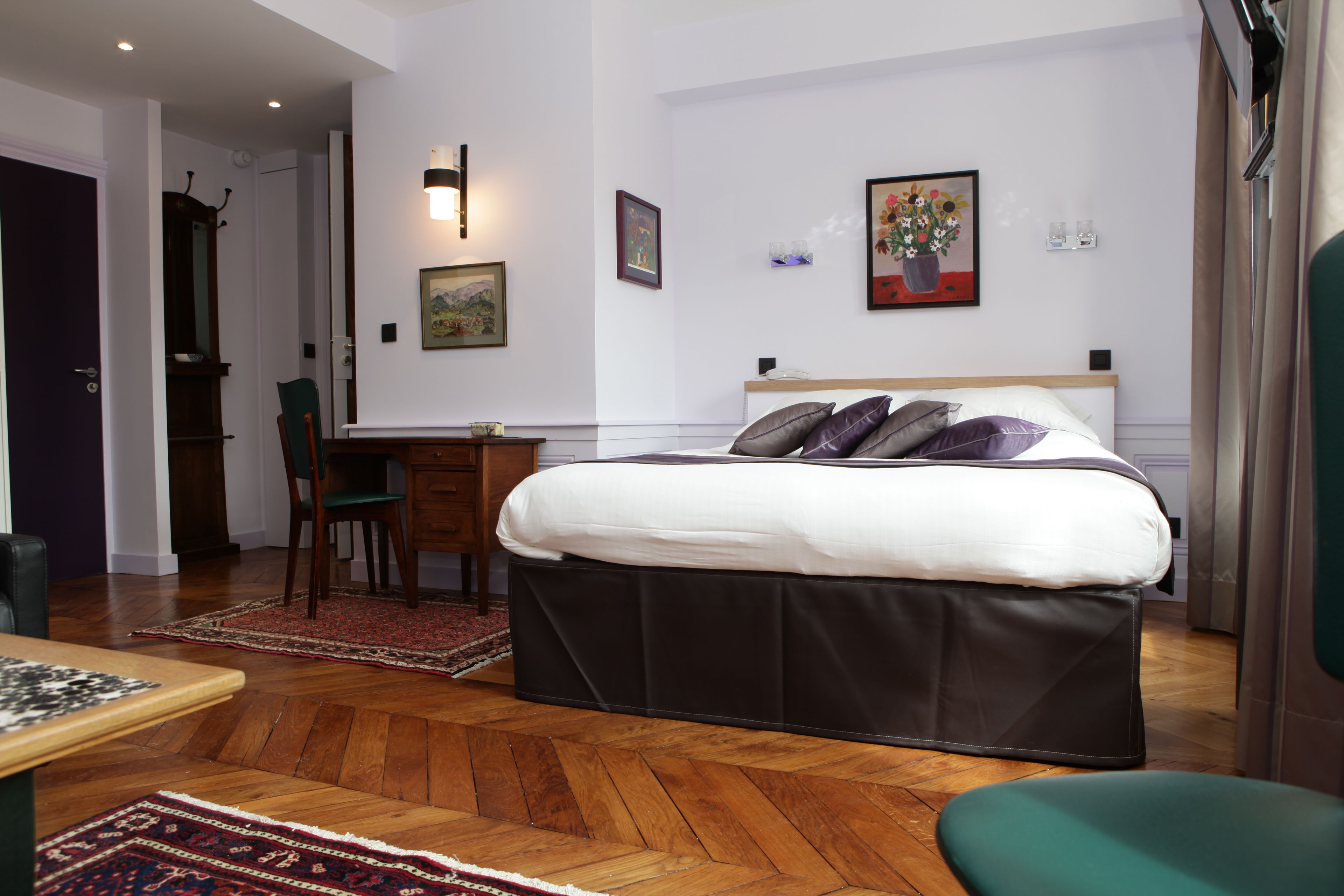 A hotel room with a bed, desk, chair, and a view of the hallway.