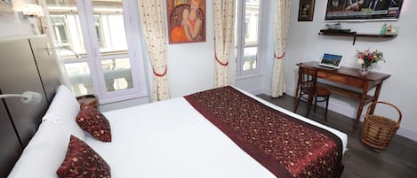 A hotel room with a bed, a desk, a television, and a window with curtains.