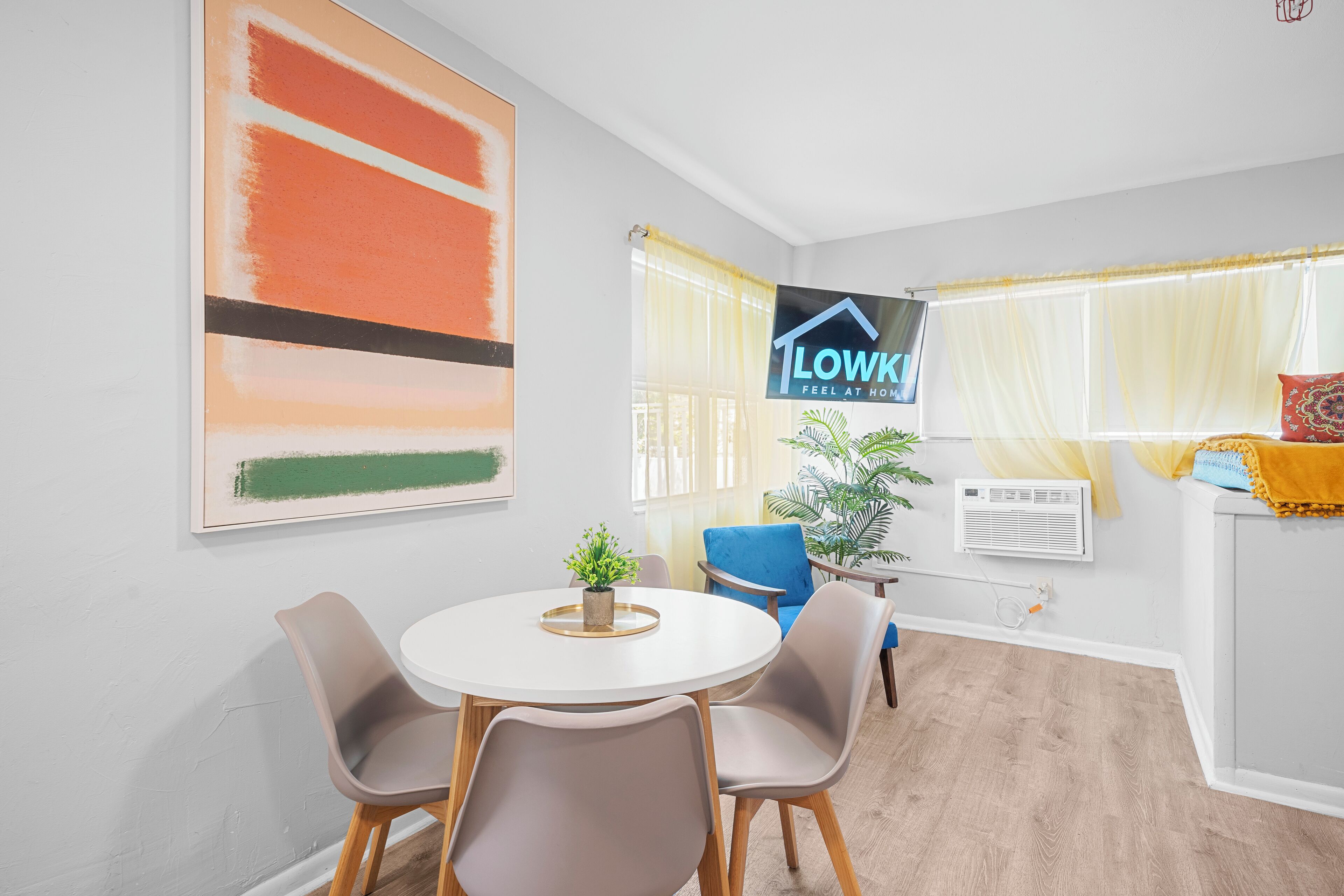 A modern living room with a round dining table, two chairs, a potted plant, and a large abstract painting.