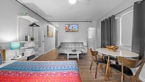 A modern, well-lit room with a bed, a sofa, a dining table with chairs, a ceiling fan, and a window with curtains. - Rock Apartments by Lowkl (Miami Beach)