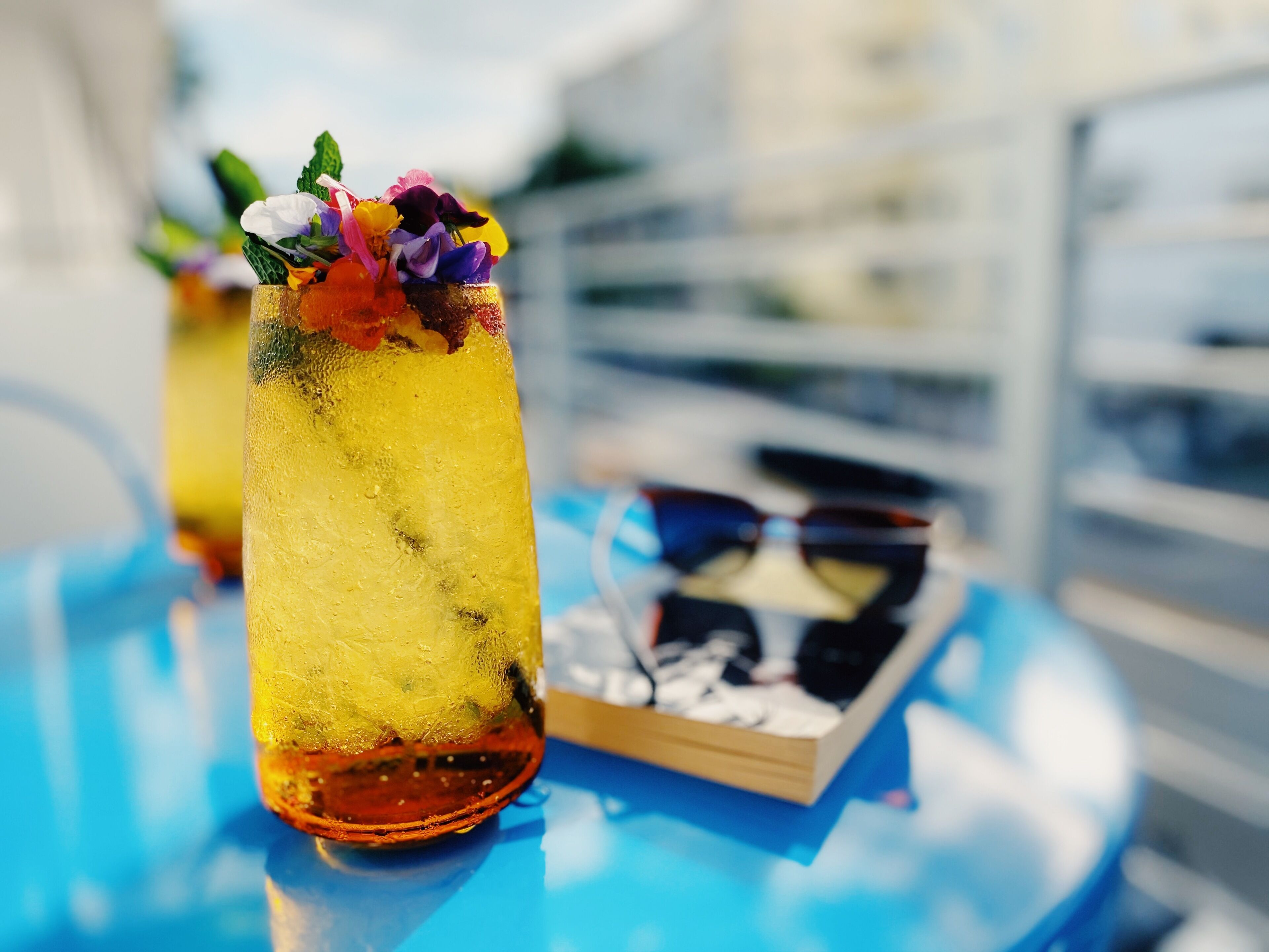A cocktail glass with a floral garnish on a reflective blue table.