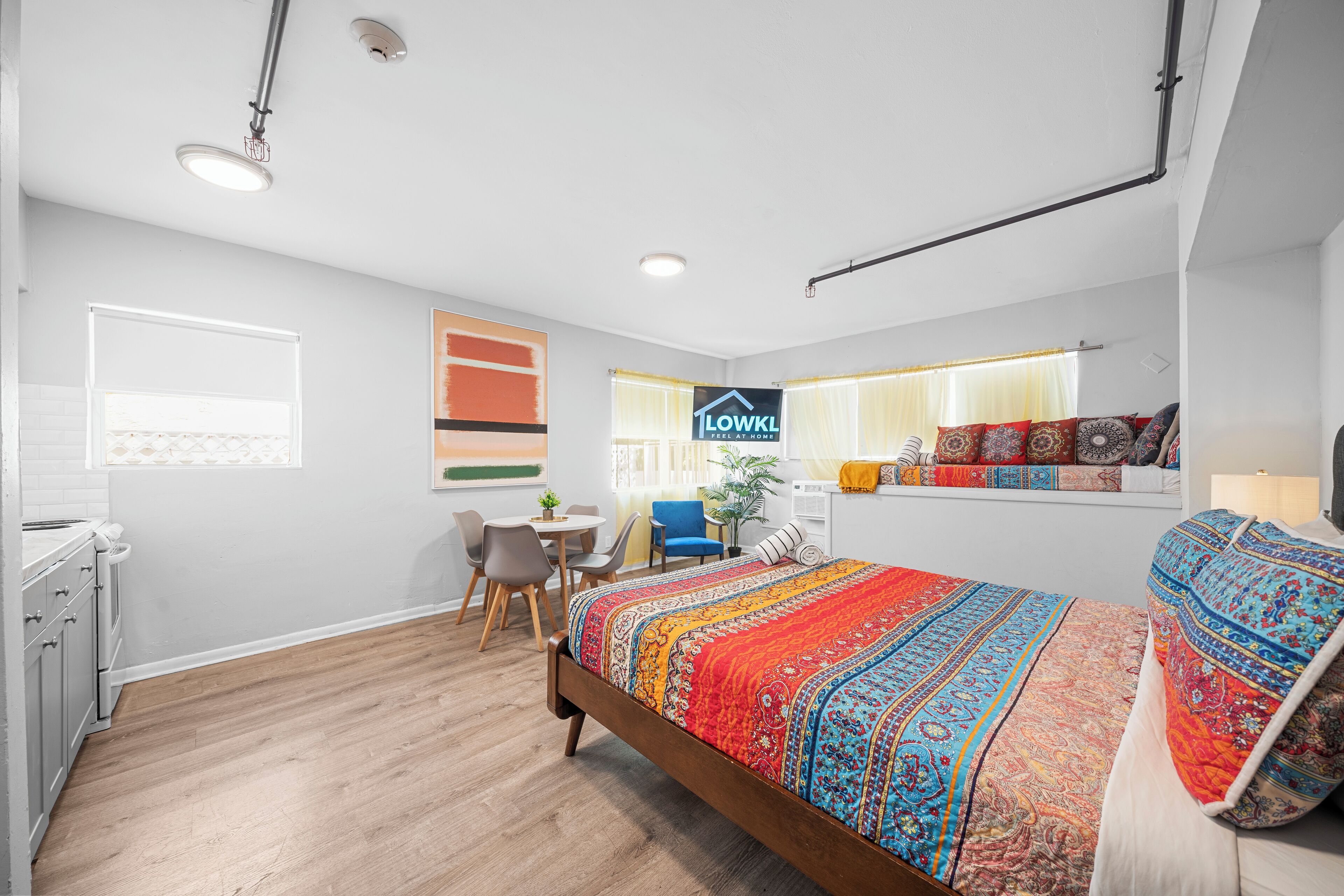A modern bedroom with a wooden bed, a desk, and a chair. There is a window with curtains and a sign on the wall.