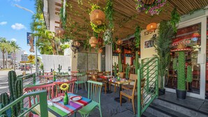 An outdoor cafe with colorful chairs and tables, surrounded by potted plants and cacti. - Rock Apartments by Lowkl (Miami Beach)