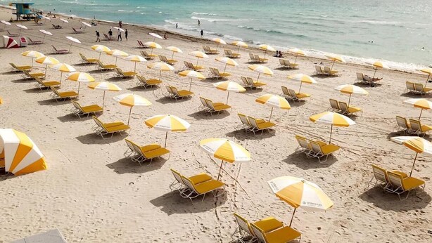 A beach with rows of yellow and white striped umbrellas and beach chairs. - Rock Apartments by Lowkl (Miami Beach)