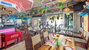 A restaurant with multiple dining tables and chairs, a Coca-Cola cooler, and hanging plants. - Rock Apartments by Lowkl (Miami Beach)