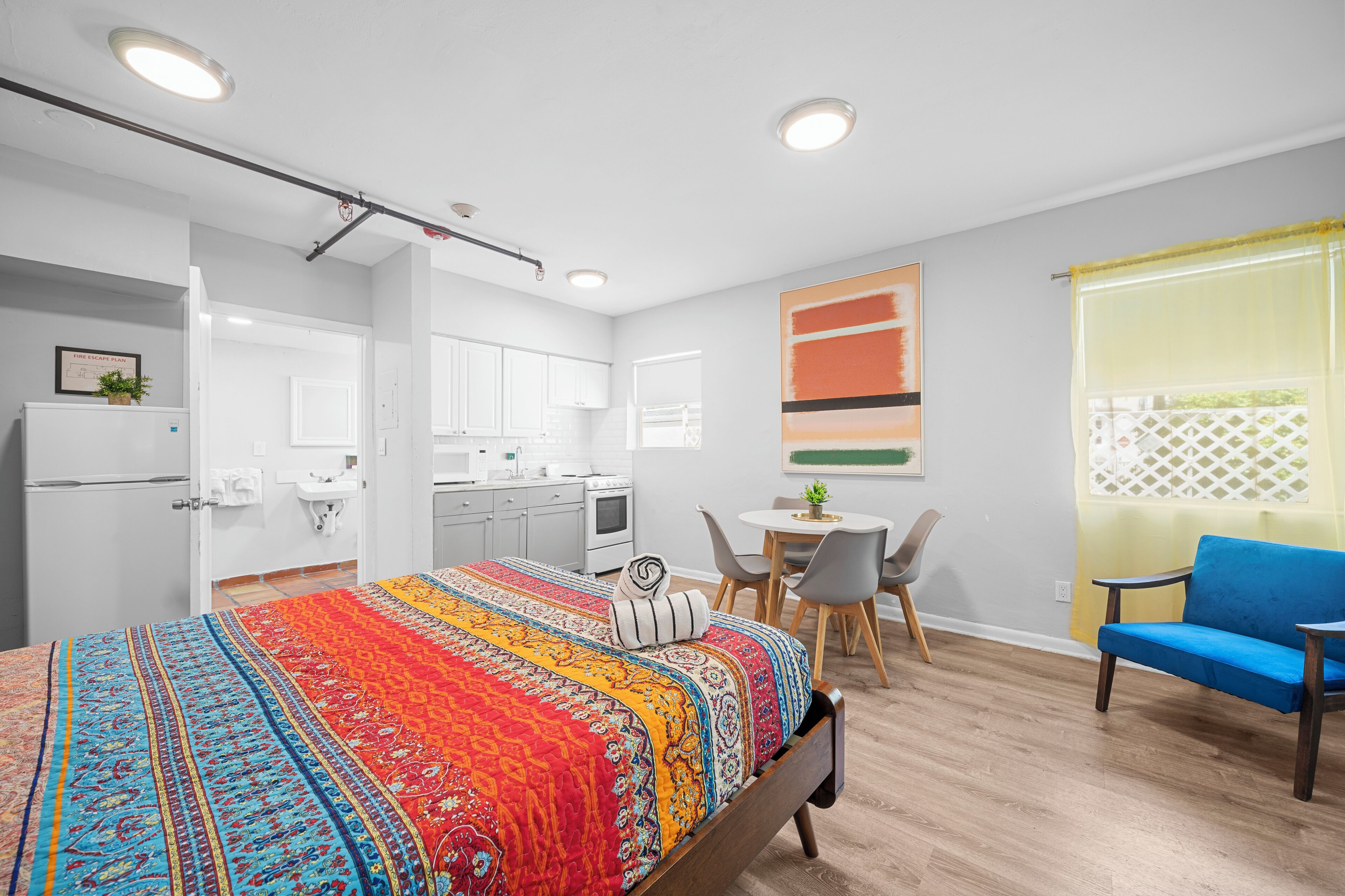 A modern hotel room with a large bed, a kitchenette, a dining area, and a view of the outdoors.