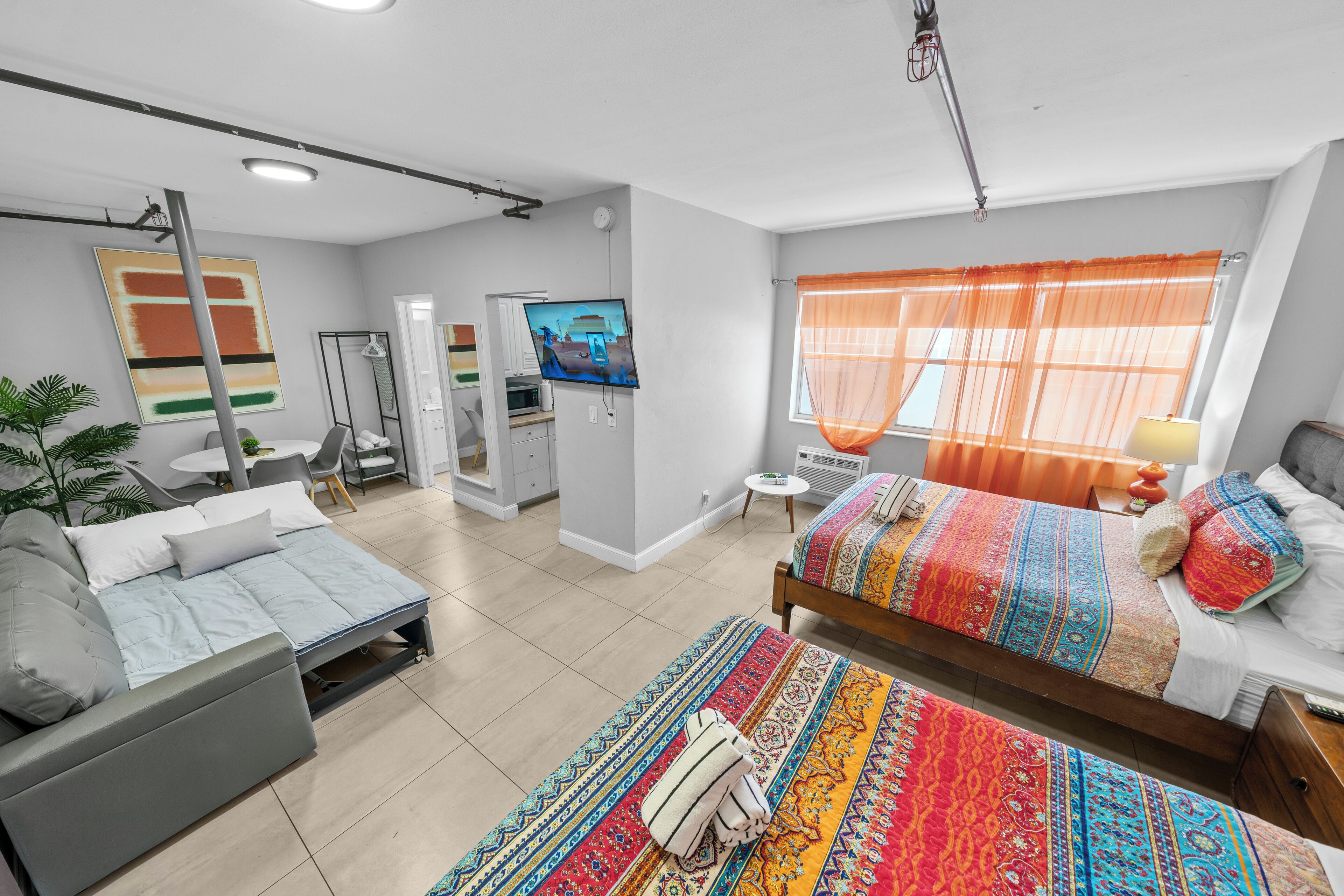 A modern hotel room with a bed, sofa, and a dining area with a TV.