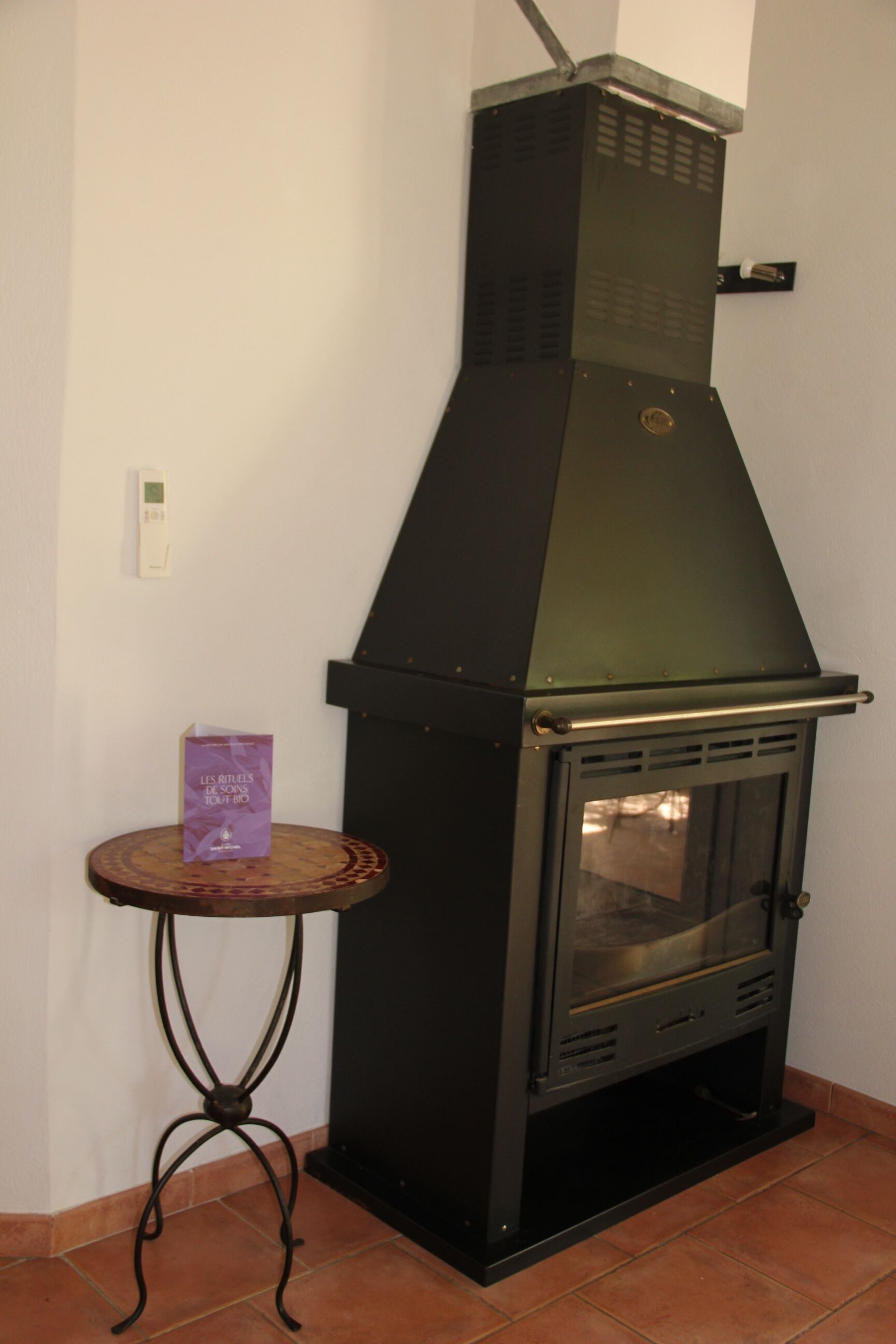 Una estufa de leña con puerta de cristal, una mesita redonda con un libro y un atril metálico.