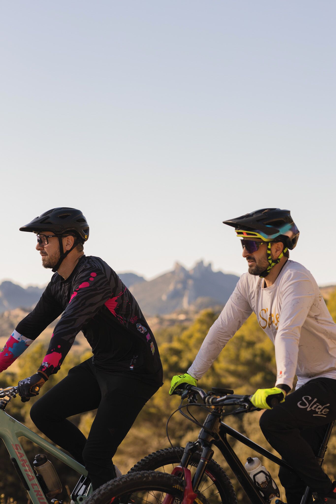 Deux cyclistes sur un sentier de VTT, avec un ciel dégagé et des montagnes à l’horizon.