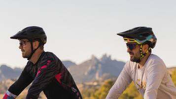 Deux cyclistes sur un sentier de VTT, avec un ciel dégagé et des montagnes à l’horizon.